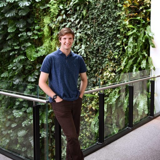 Profile picture of Alec Christie standing against the backdrop of a green living wall with plants.